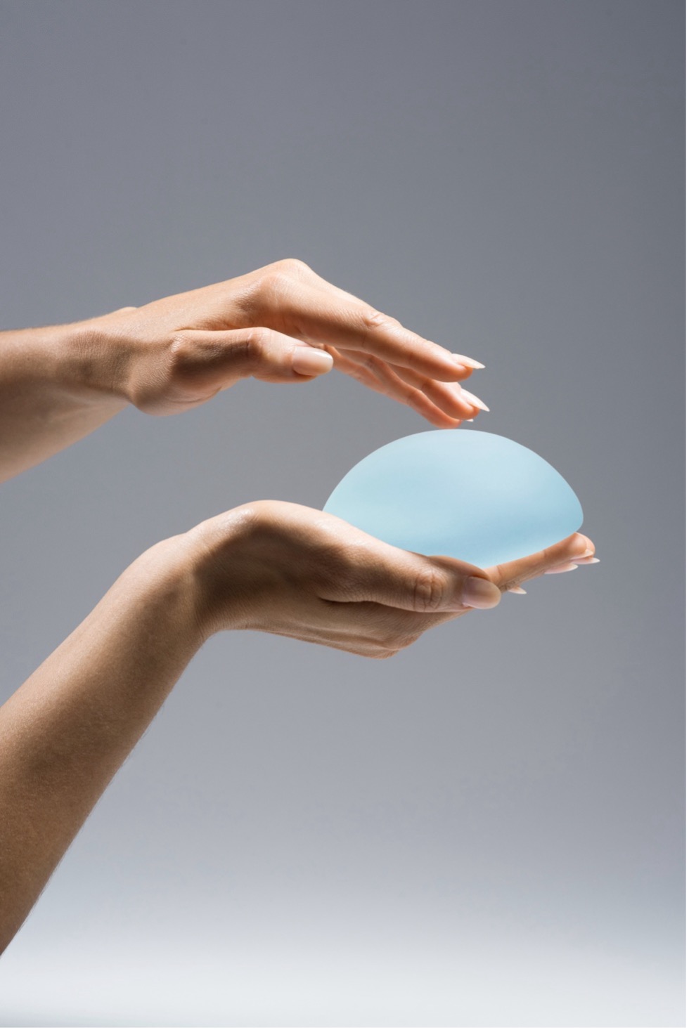 Hands gently holding a blue Motiva silicone breast implant